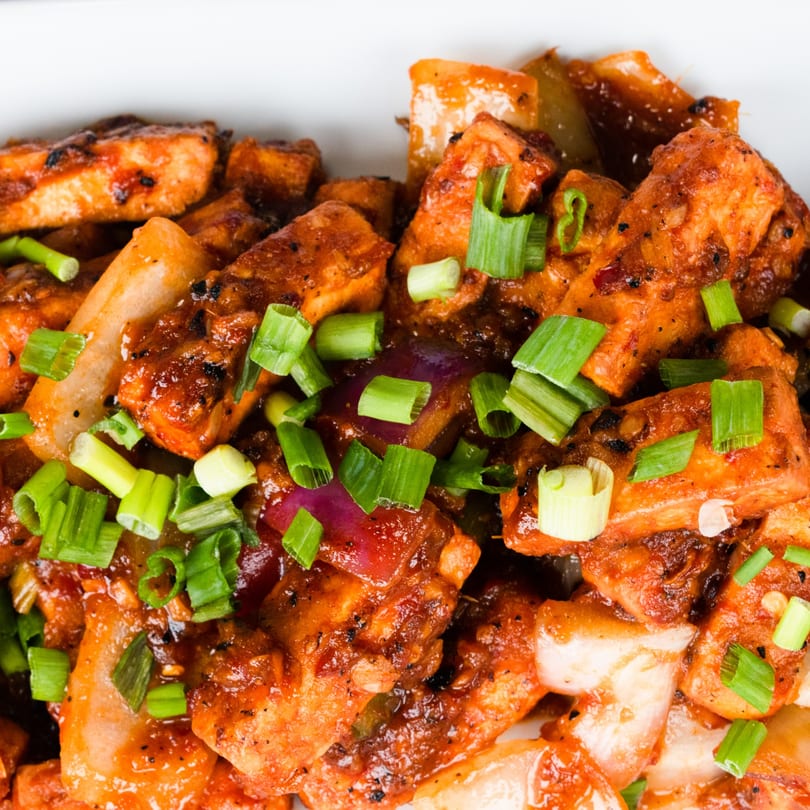 Close-up of Indian chili paneer, featuring fried paneer cubes in a spicy red sauce with green onions.