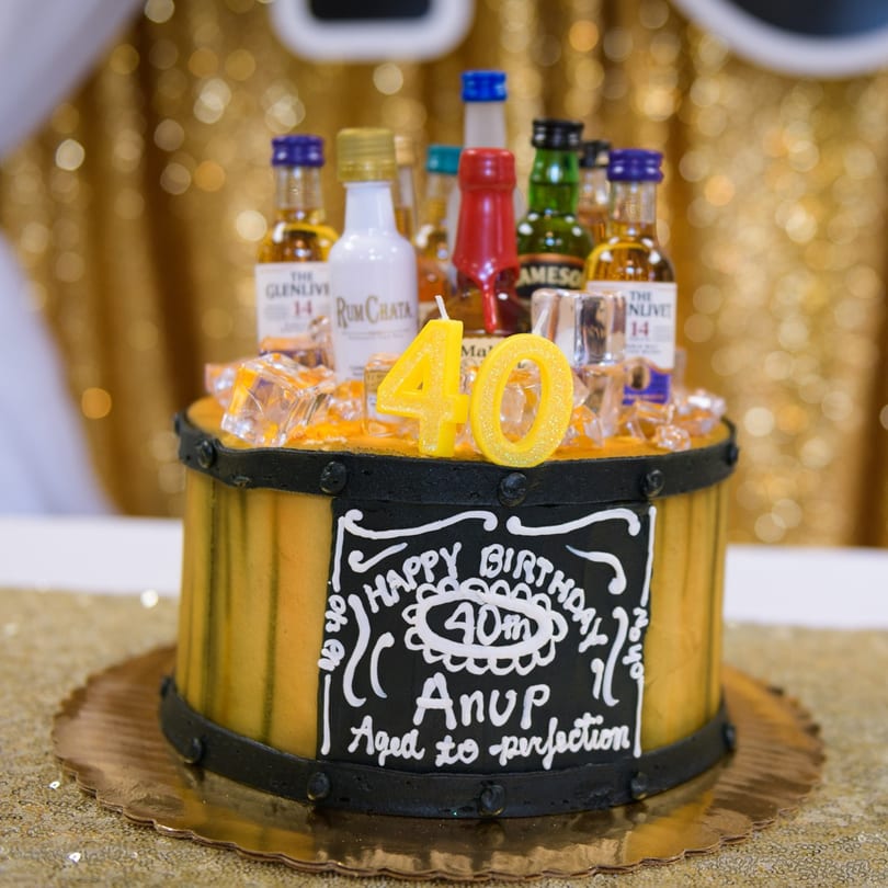 A barrel-shaped birthday cake with miniature liquor bottles, ice cubes, and "40" candles on top.