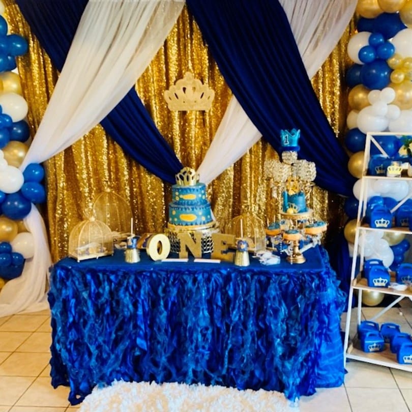 Blue and gold themed party decorations with a cake, cupcakes, and balloons for a first birthday.