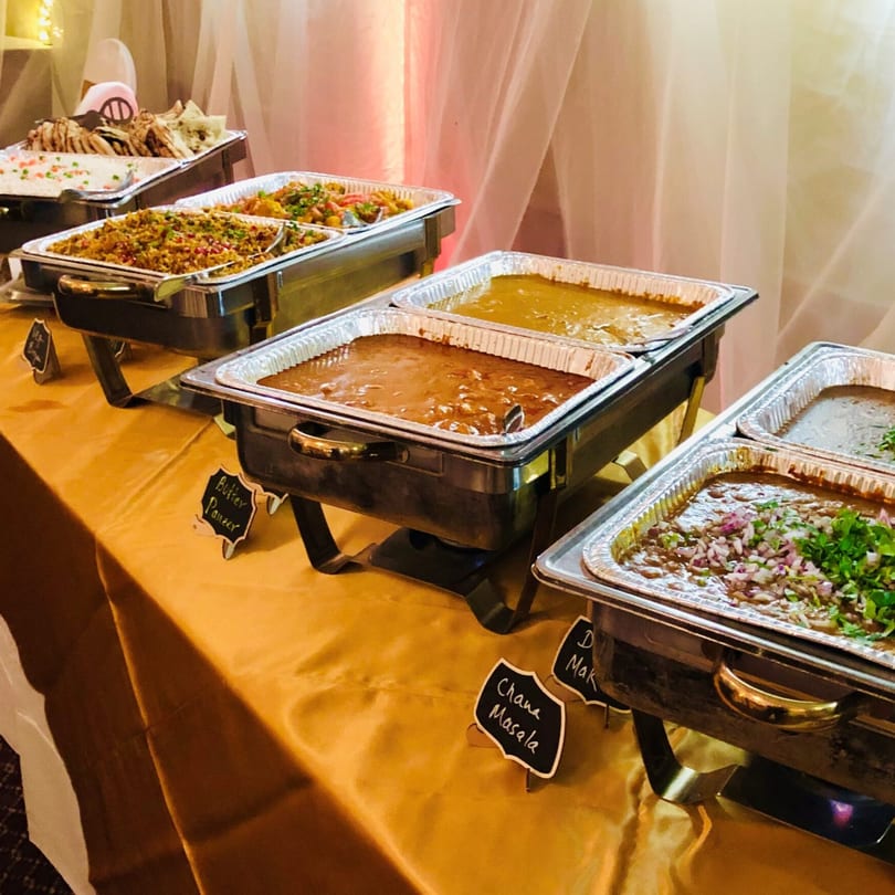 A buffet of Indian dishes, including Butter Paneer and Chana Masala, in chafing dishes.