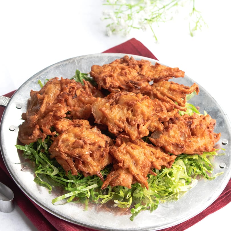 Crispy golden-brown Indian pakora appetizers, served on a bed of shredded lettuce on a silver platter.