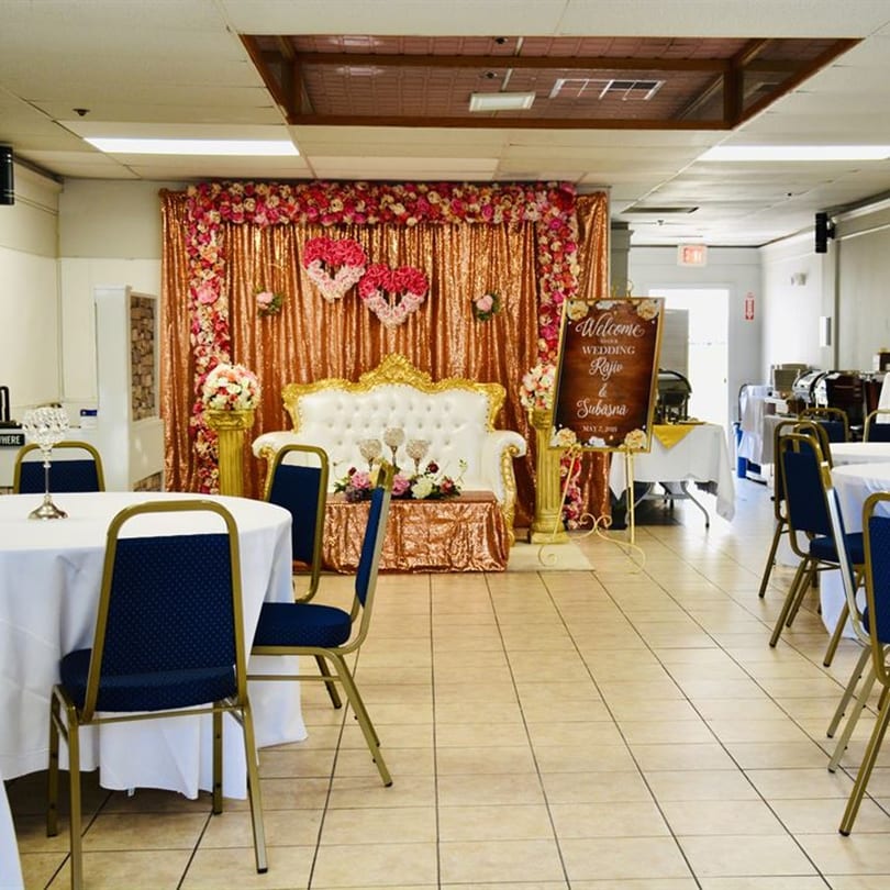 A banquet hall set up for a wedding reception with a golden sequin backdrop and white sofa.