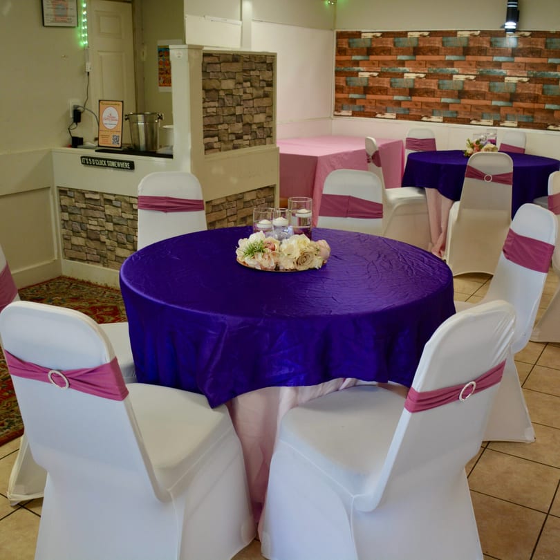 Himalayan Curry House dining room with purple and pink tablecloths, white chairs, and floral centerpieces.